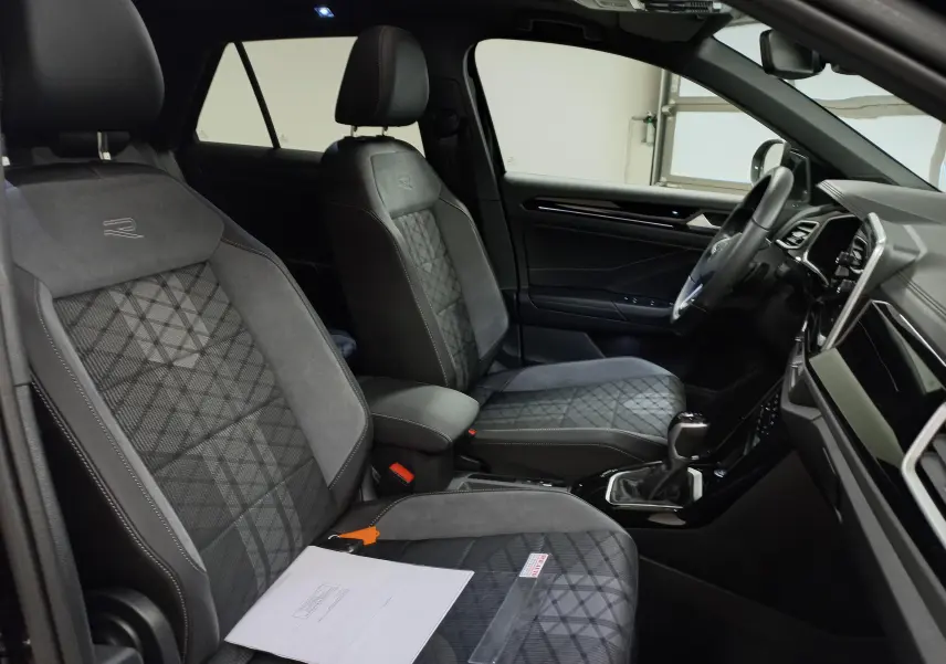 Vue intérieure côté droit du Volkswagen T-Roc 2025, sièges avant en tissu noir avec surpiqûres et logo R brodé.