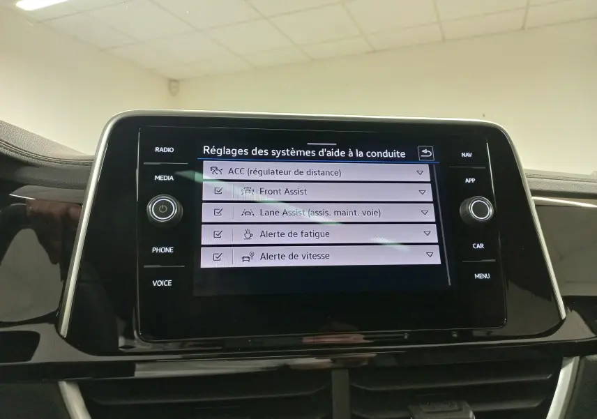 Écran tactile central du Volkswagen T-Roc 2025 affichant les réglages des aides à la conduite, intérieur noir.