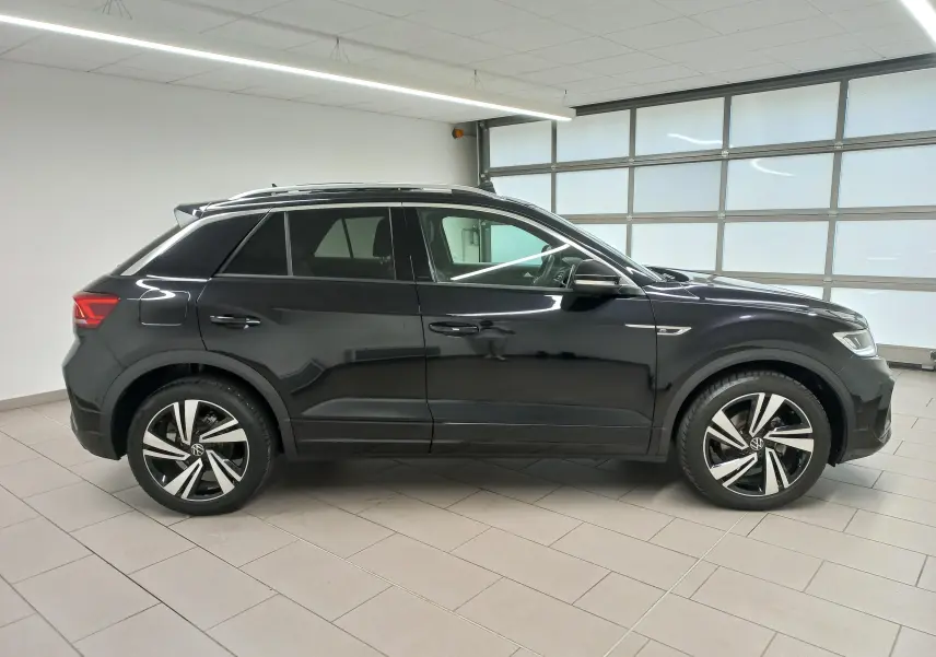 Vue de profil côté gauche d’un Volkswagen T-Roc noir intense 2025 avec jantes alliage et toit ouvrant panoramique.