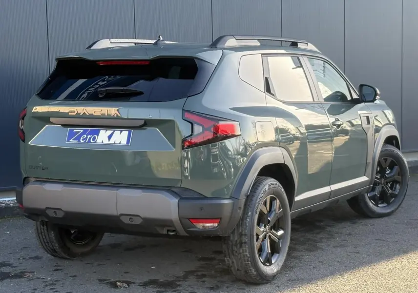 Vue 3/4 arrière droite du Dacia Duster 2026 kaki lichen avec jantes noires et barres de toit longitudinales.