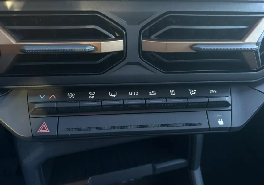 Vue rapprochée de la console centrale du Dacia Duster 2026, boutons de climatisation et aérateurs noirs avec inserts bronze.