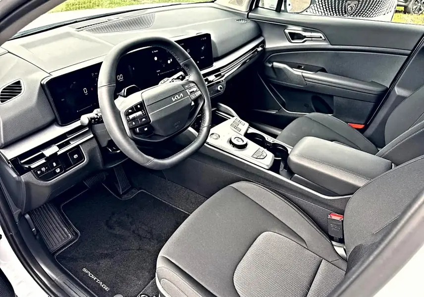 Vue intérieure côté conducteur du Kia Sportage 1.6 hybride blanc, avec volant multifonction et écran tactile large.