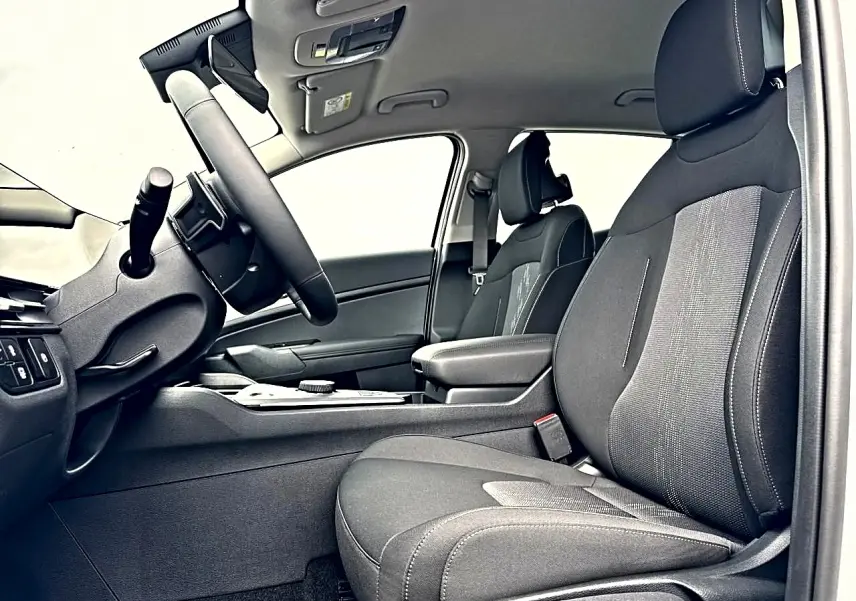 Vue intérieure côté conducteur du Kia Sportage 1.6 hybride 239 active, sièges noirs et accoudoir central avec rangement.