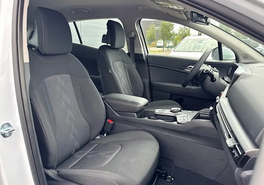 Vue intérieure côté conducteur du Kia Sportage blanc 2026, montrant les sièges avant noirs et la console centrale avec accoudoir.