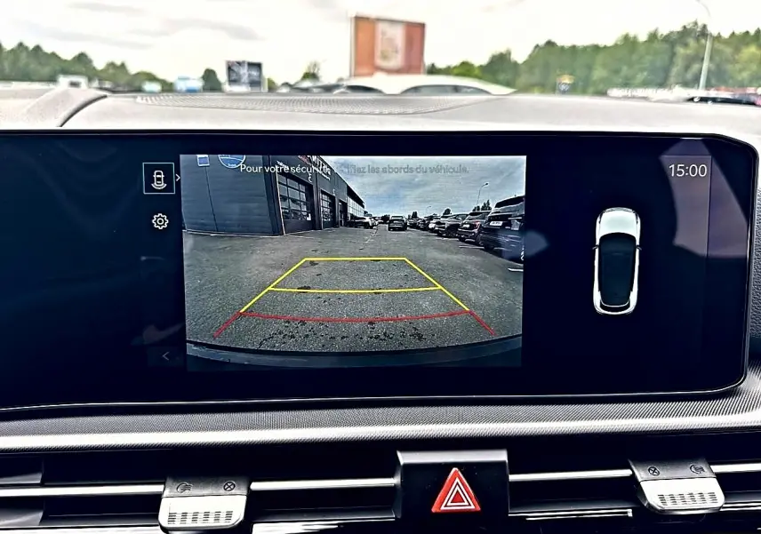 Écran tactile intérieur montrant la caméra de recul d’un KIA SPORTAGE blanc hybride, vue arrière en stationnement.