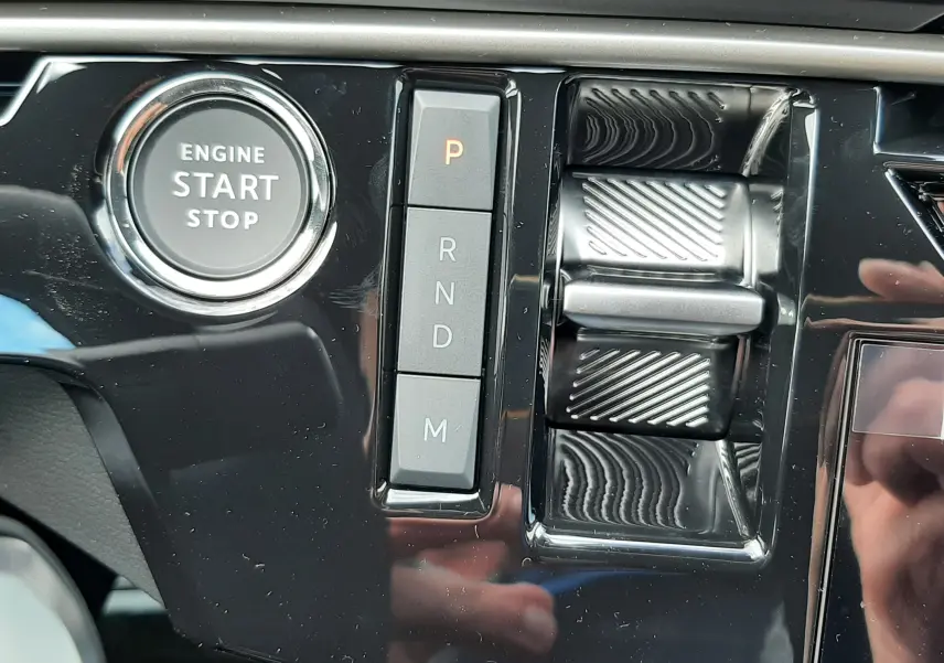 Gros plan sur la console centrale noire brillante du Peugeot 3008 1.2 Hybrid 145ch GT avec bouton start/stop et commandes de boîte auto.