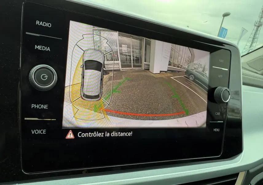 Vue de la caméra de recul du Volkswagen T-Roc argent pyrite métallisé montrant l'arrière et un parking adjacent.