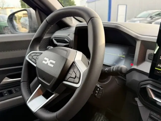 Vue rapprochée du volant multifonction noir du Dacia Duster 1.8 Hybrid 155 Journey avec tableau de bord numérique.