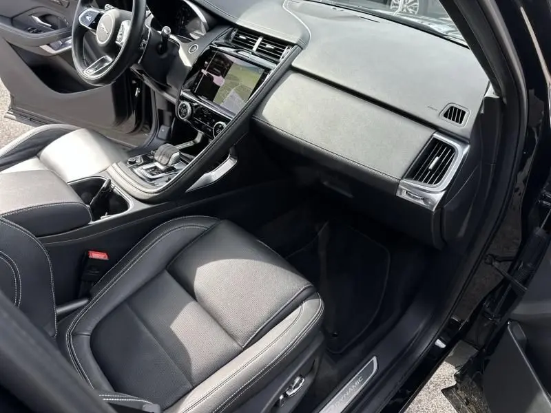 Vue intérieure côté passager de la Jaguar E-PACE noire 2021, mettant en valeur le tableau de bord et les sièges cuir noirs.