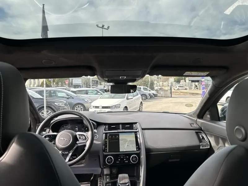 Vue intérieure avant du Jaguar E-PACE noir 2021, mettant en valeur le tableau de bord moderne et le toit panoramique.