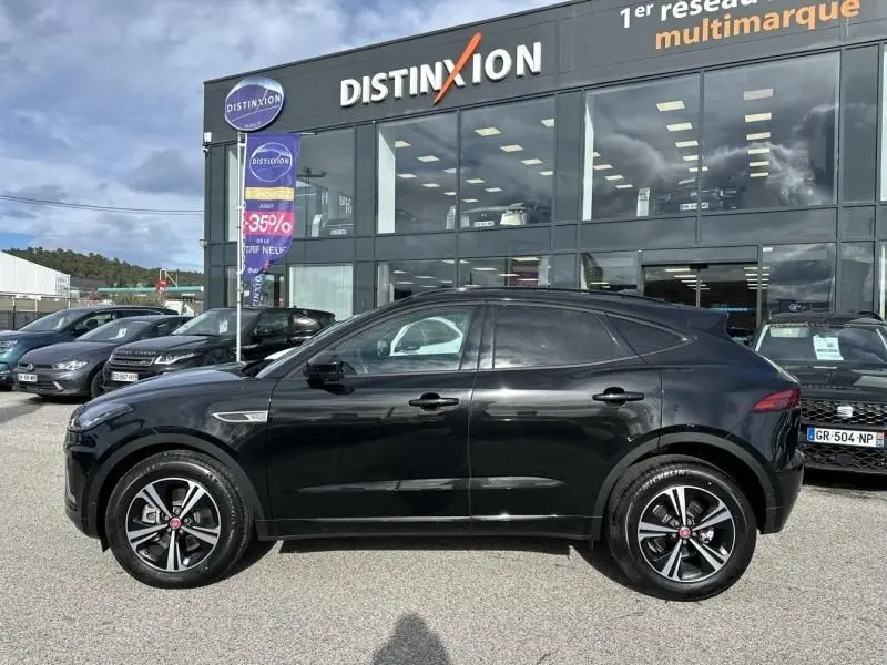 Jaguar E-PACE noir vue de profil côté gauche, SUV compact avec jantes alliage distinctives, stationné devant un concessionnaire.