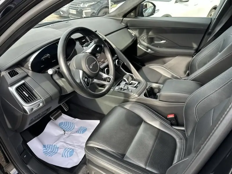 Vue intérieure côté conducteur du Jaguar E-PACE noir 2021, mettant en valeur le volant, les sièges en cuir et la console centrale.