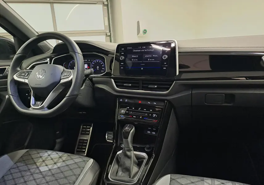 Vue intérieure avant du Volkswagen T-Roc 2025, tableau de bord noir avec écran tactile central et volant multifonction.