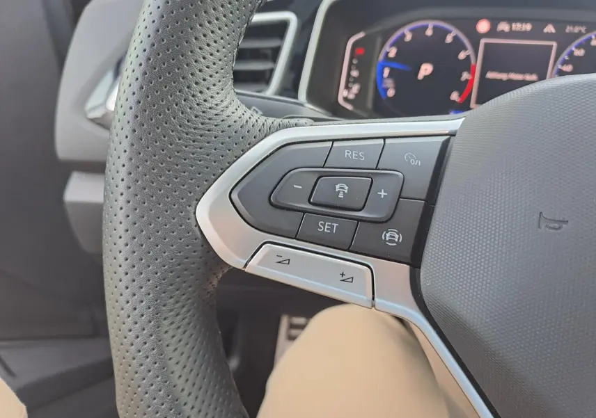 Gros plan sur le côté gauche du volant perforé du Volkswagen T-Roc 2025 avec commandes de régulateur adaptatif.
