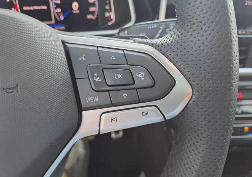 Gros plan sur les commandes multifonctions à gauche du volant perforé du Volkswagen T-Roc 2025 finition R-Line.