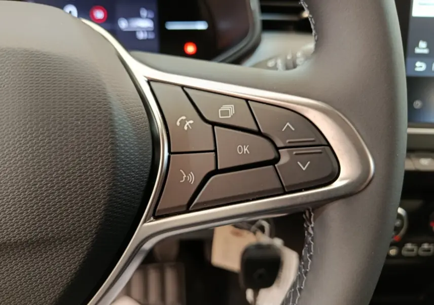 Gros plan sur les commandes multifonctions à droite du volant cuir de la Renault Clio blanche 2024, avec affichage numérique en arrière-plan.