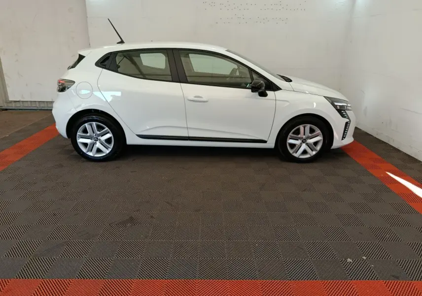 Renault Clio blanc vue de profil côté gauche dans un garage avec éclairage intérieur et sol à damier noir et rouge.
