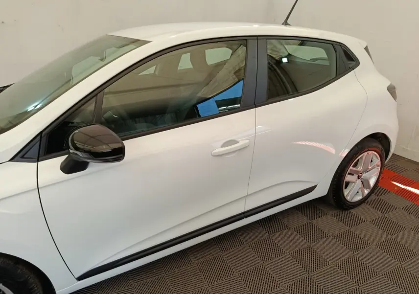 Profil côté gauche de la Renault Clio blanche 2024 avec rétroviseur noir et jantes alliage visibles en intérieur neutre.