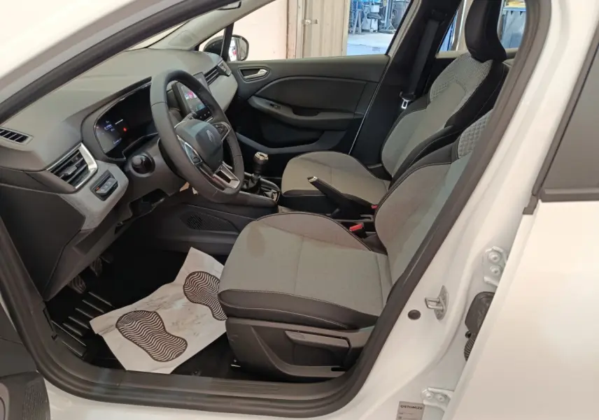 Intérieur de la Renault Clio blanc 2024, vue côté conducteur, sièges gris et tableau de bord moderne avec écran tactile.