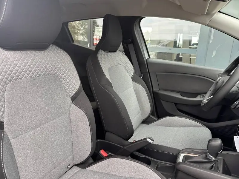 Vue intérieure côté conducteur de la Renault Clio 2025, sièges tissu gris avec surpiqûres et levier de vitesse manuel.