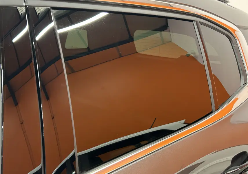 Gros plan sur la vitre arrière côté droit d'un Citroën C5 Aircross gris platinium avec reflet intérieur orangé.