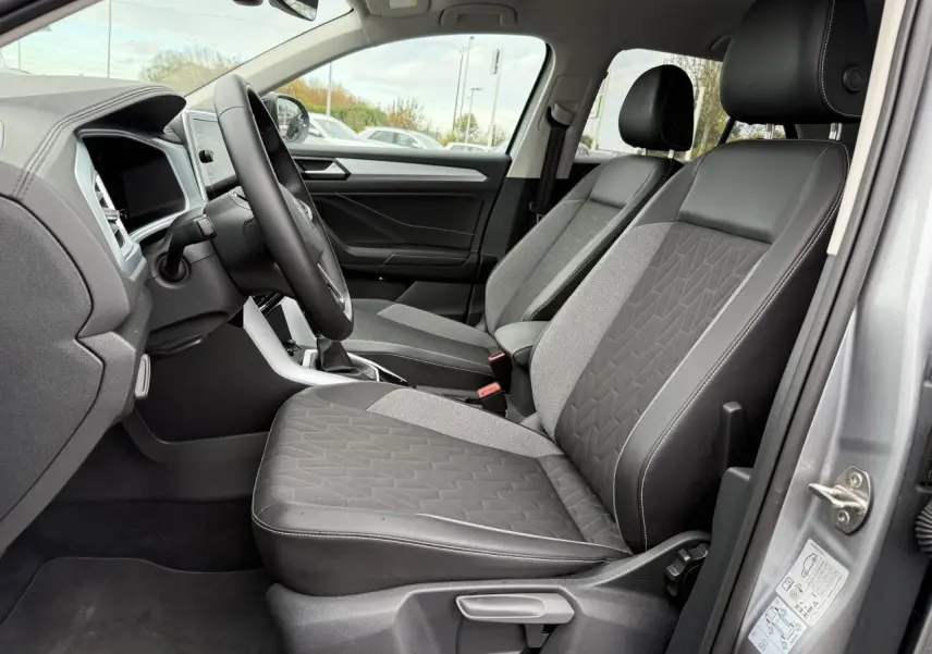 Intérieur côté conducteur du Volkswagen T-Roc argent, montrant les sièges avant en tissu et cuir avec console centrale.