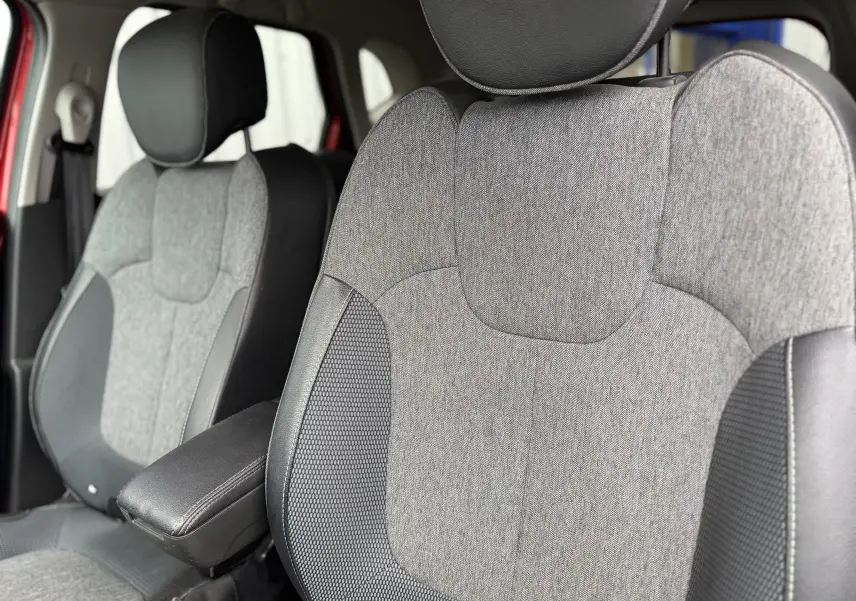 Gros plan sur les sièges avant gris et noir du Renault Captur rouge, mettant en valeur l'accoudoir central et les textures du tissu.