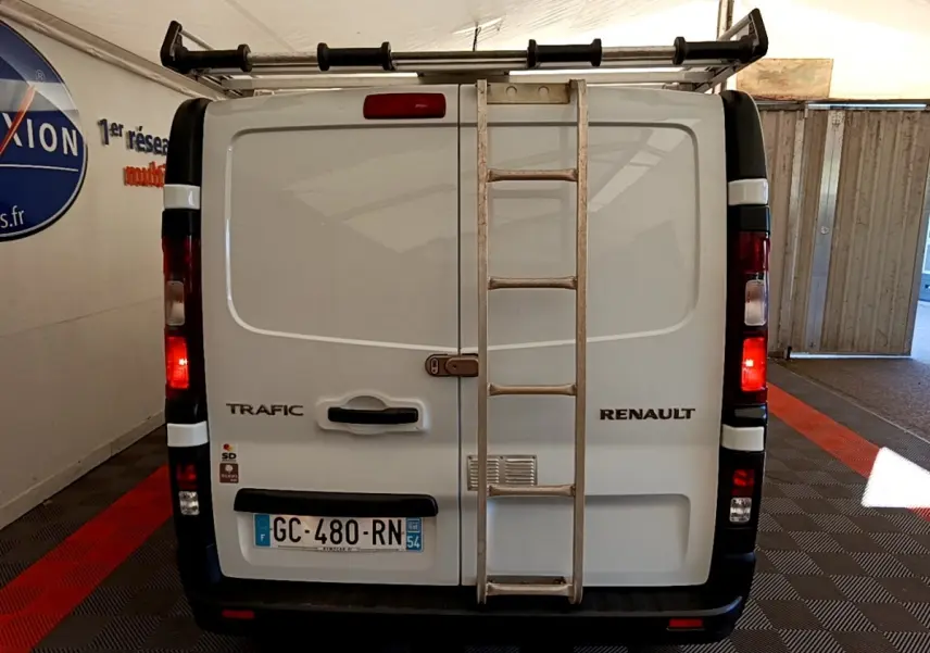 Vue arrière du Renault Trafic Fourgon blanc avec échelle métallique fixée sur la porte et feux arrière allumés.