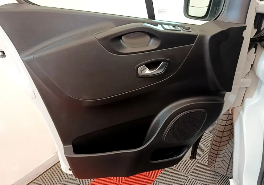 Vue rapprochée de la porte avant droite noire du Renault Trafic Fourgon blanc, avec poignée et haut-parleur intégrés.