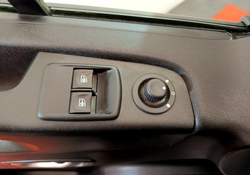 Gros plan sur les commandes de lève-vitres et réglage des rétroviseurs côté conducteur du Renault Trafic Fourgon blanc.
