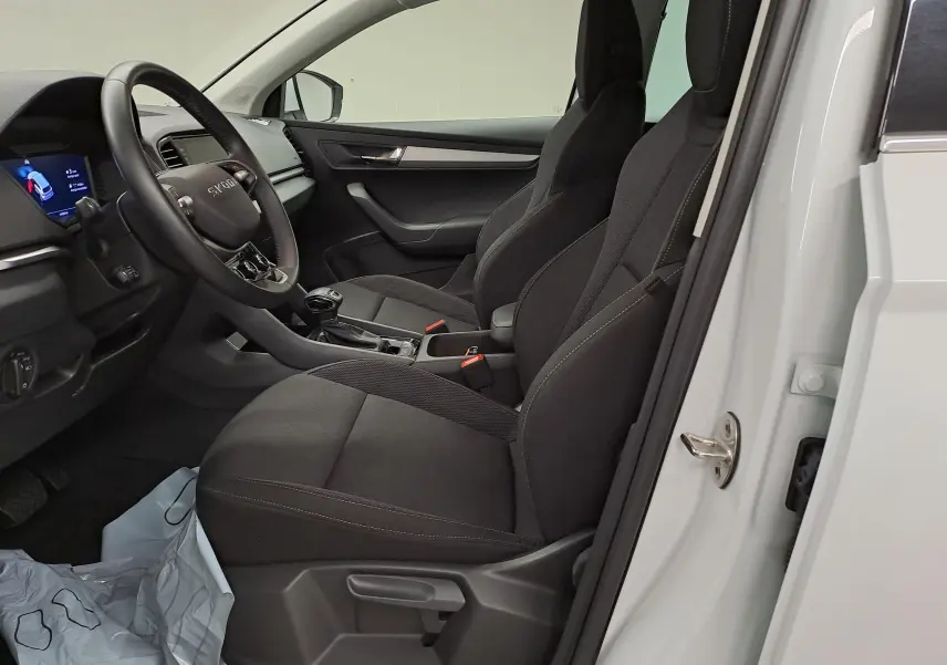 Vue intérieure côté conducteur du Skoda Karoq blanc Lune 2025, sièges noirs et tableau de bord moderne avec volant multifonction.