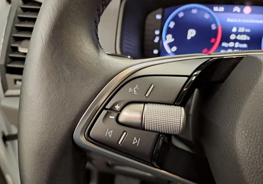 Gros plan sur les commandes du volant du Skoda Karoq blanc Lune 2025 avec molette métallique et tableau de bord numérique.