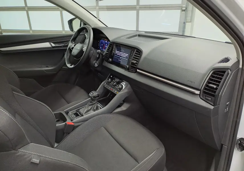Vue intérieure côté conducteur du Skoda Karoq 2025, tableau de bord moderne avec écran tactile et sièges noirs tissu.