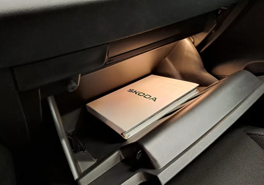Gros plan sur la boîte à gants ouverte d'un Skoda Karoq blanc Lune, avec manuel d'utilisation visible à l'intérieur.