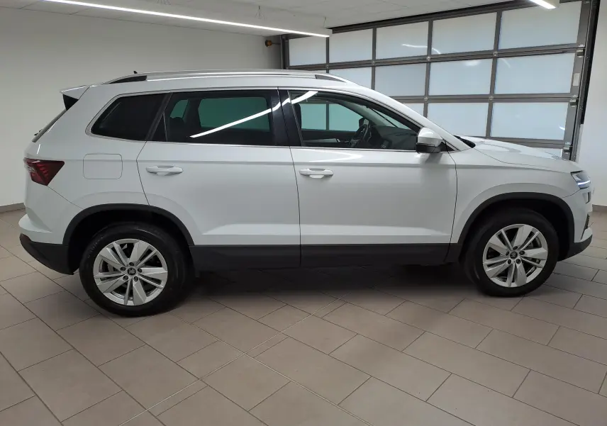 Vue de profil côté gauche du Skoda Karoq blanc Lune 2025 avec pack chrome extérieur et rampes de pavillon argent.