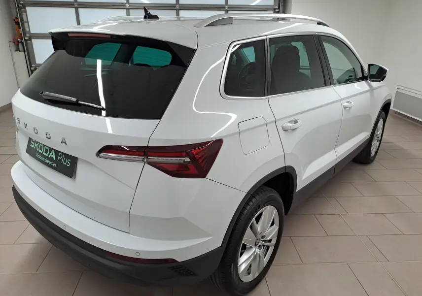 Vue 3/4 arrière droite du Skoda Karoq blanc Lune avec rampes de pavillon argent et entourage de vitres chromé.
