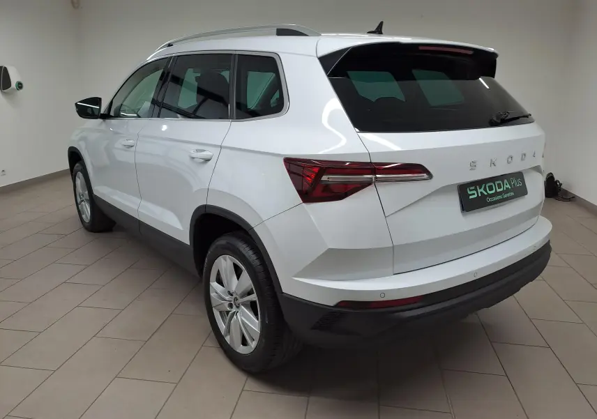 Vue 3/4 arrière droite du Skoda Karoq blanc Lune avec spoiler arrière, rampes de pavillon argent et entourage de vitres chromé.