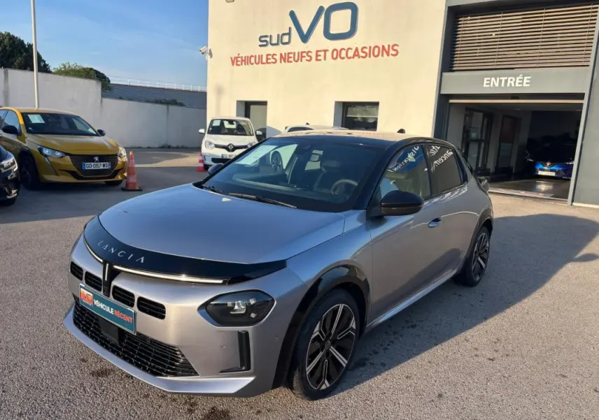 Lancia Ypsilon gris vue 3/4 avant droit, avec jantes 17 pouces et calandre noire brillante, stationnée devant un garage.