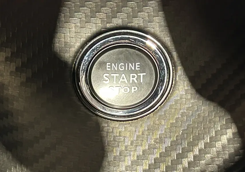 Gros plan sur le bouton start/stop moteur entouré d’un décor en fibre de carbone à l’intérieur du Peugeot 2008 gris Artense.