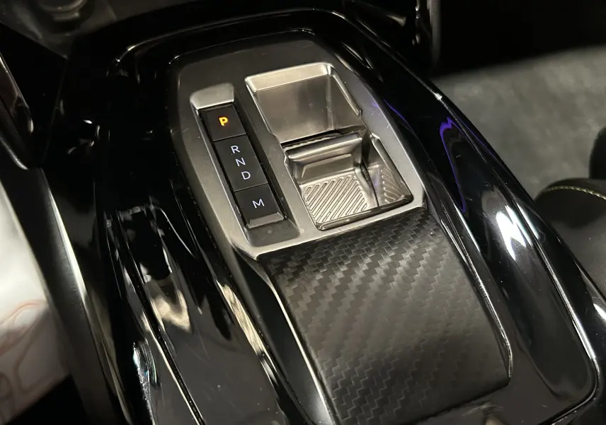 Gros plan sur la console centrale noire brillante du Peugeot 2008 2024 avec sélecteur de boîte auto et finition carbone.