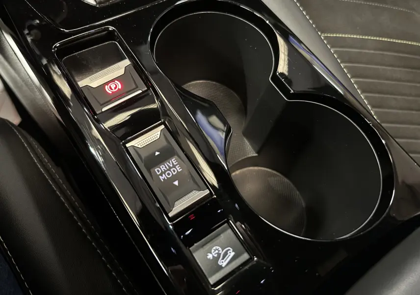 Gros plan sur la console centrale noire brillante du Peugeot 2008 2024 avec boutons frein à main, mode de conduite et assistance descente.