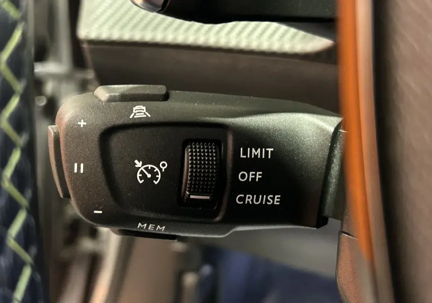 Gros plan sur la commande de régulateur de vitesse au volant du Peugeot 2008 gris Artense, avec molette et inscriptions blanches.