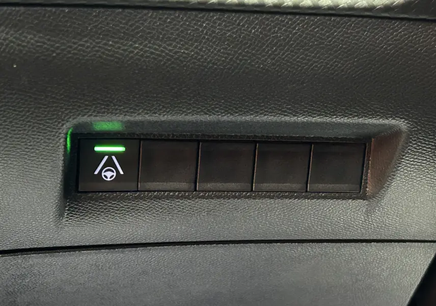 Bouton de commande d'aide au maintien de voie avec témoin vert sur tableau de bord noir du Peugeot 2008 gris Artense.