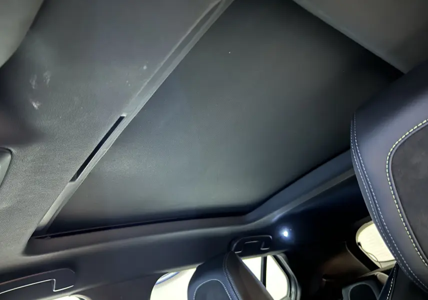 Vue intérieure du toit ouvrant panoramique fermé et siège avant droit en cuir noir avec surpiqûres vertes dans un Peugeot 2008 Gris Artense 2024.