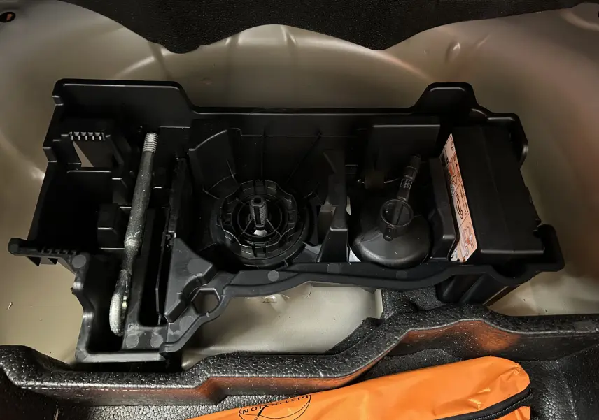 Vue rapprochée du compartiment à outils sous le plancher du coffre du Peugeot 2008 gris Artense, avec support plastique et accessoires.