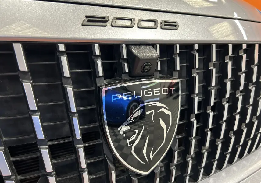 Gros plan sur la calandre gris Artense du Peugeot 2008 2024 avec logo lion et caméra frontale intégrée.