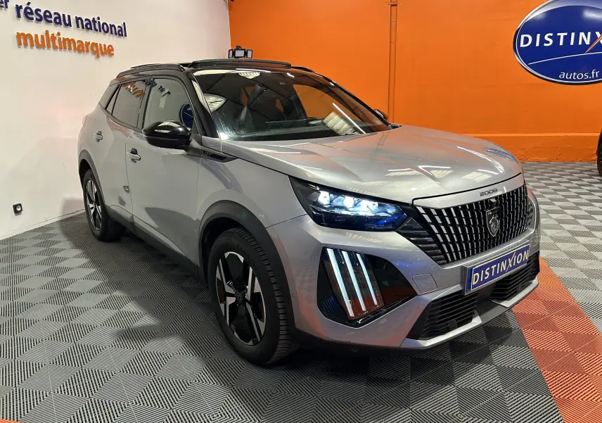 Peugeot 2008 Gris Artense en 3/4 avant droit, avec phares LED allumés et toit ouvrant panoramique visible.