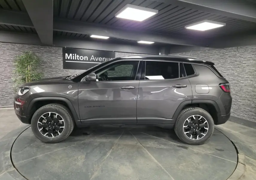 Vue de profil côté gauche d’un Jeep Compass gris métallisé avec toit noir et jantes noires en showroom.