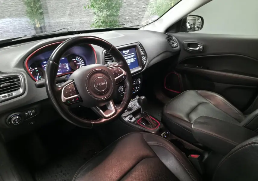 Vue intérieure côté conducteur de la Jeep Compass Trailhawk 2020, sellerie cuir noire avec surpiqûres rouges et tableau de bord moderne.