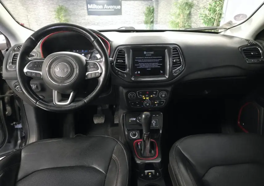 Vue intérieure du tableau de bord et volant noir du Jeep Compass Trailhawk 2020 avec écran tactile central et détails rouges.
